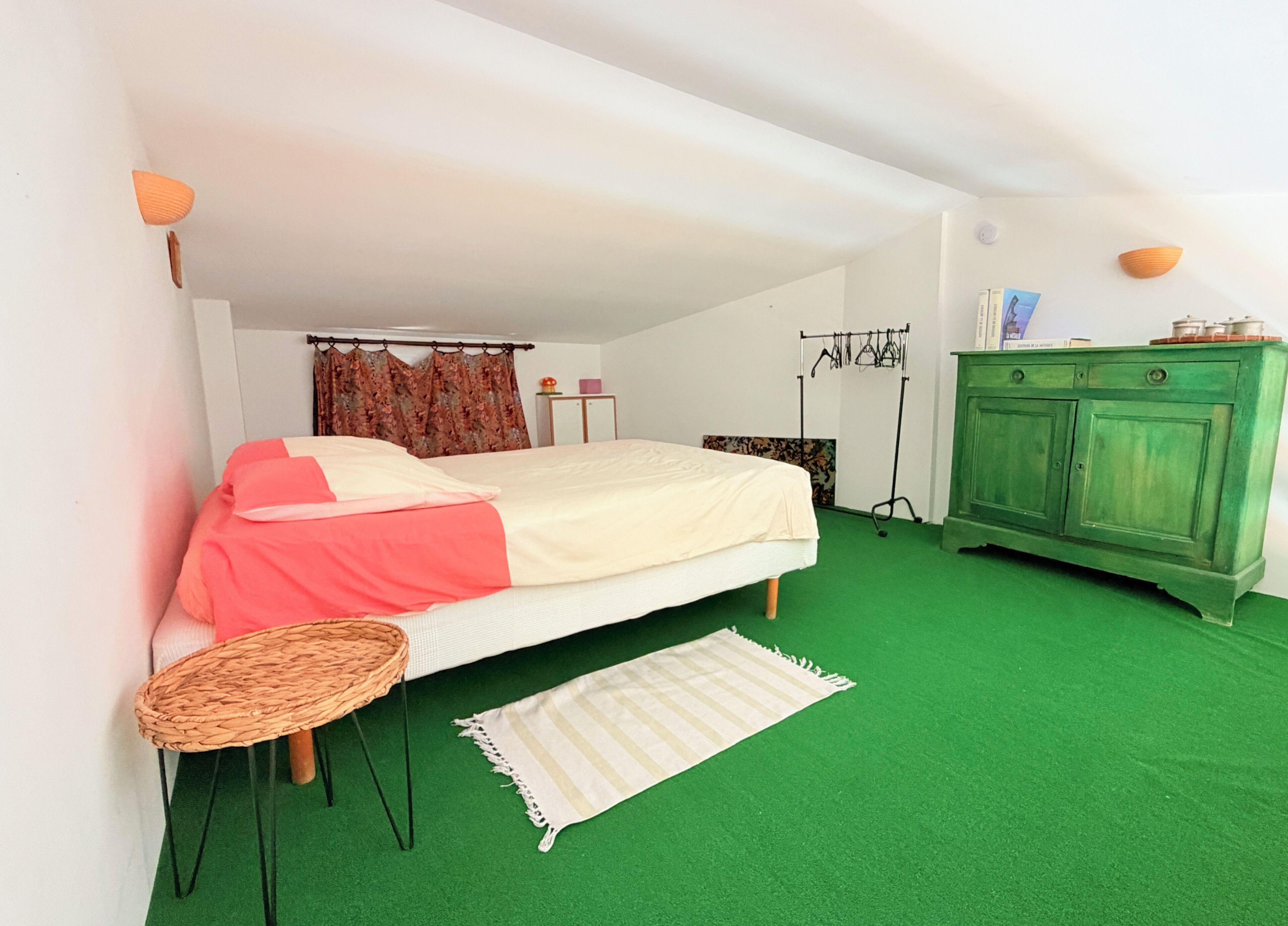 Une chambre à coucher avec un lit, une moquette verte, une petite table ronde, une armoire et un rideau.
