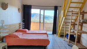 A bedroom with two beds, a wooden headboard, a bedside table with a lamp, a view of mountains through a sliding door, and a wooden ladder against the wall. - Villa, (14 p), panoramic view of the hills. Large infinity pool.  (Le Plan-de-la-Tour)