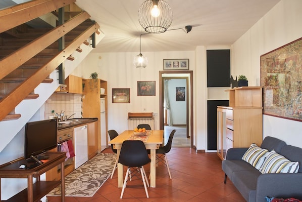 Un coin repas avec une table et des chaises en bois, une cuisine avec des meubles en bois, un escalier et un salon avec un canapé.