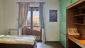 Un dormitorio con cama, ventana con cortinas, radiador, armario verde y un cuadro en la pared.