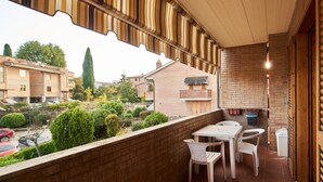 Un balcón con pared de ladrillo, una mesa con sillas, un aplique colgante y vista al vecindario.