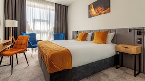 A hotel room with a bed, a desk, two chairs, a nightstand, and a painting on the wall. - Hotel Sante (Warsaw)