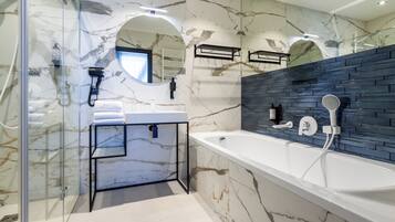 Un baño moderno con pared de mármol, cabina de ducha de vidrio, bañera blanca y toallero negro.