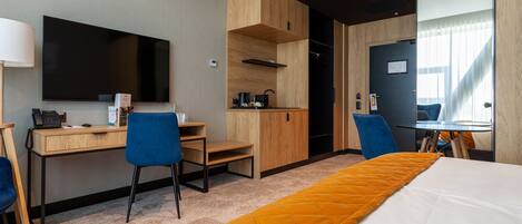 Una habitación de hotel con cama, escritorio, silla, televisor y kitchenette.