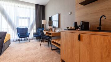Una habitación de hotel moderna con un escritorio de madera, dos sillas, un sofá, un televisor y una cafetera.