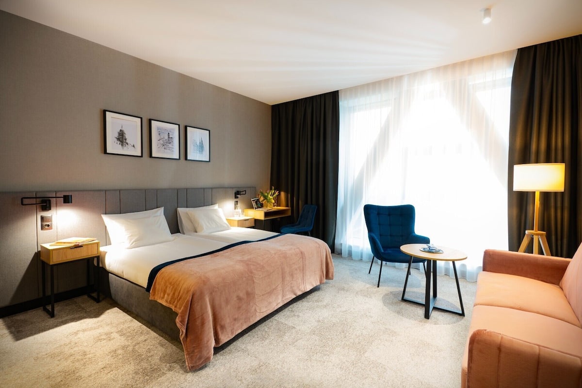 Ett hotellrum med en säng, ett skrivbord, en stol, en soffa och en lampa.