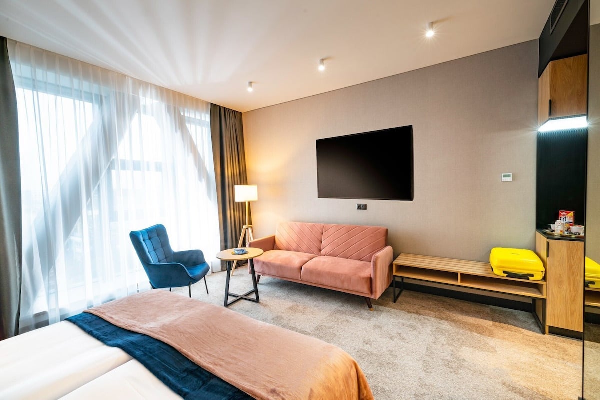 Ett hotellrum med en säng, en soffa, en stol, en tv och ett litet bord.