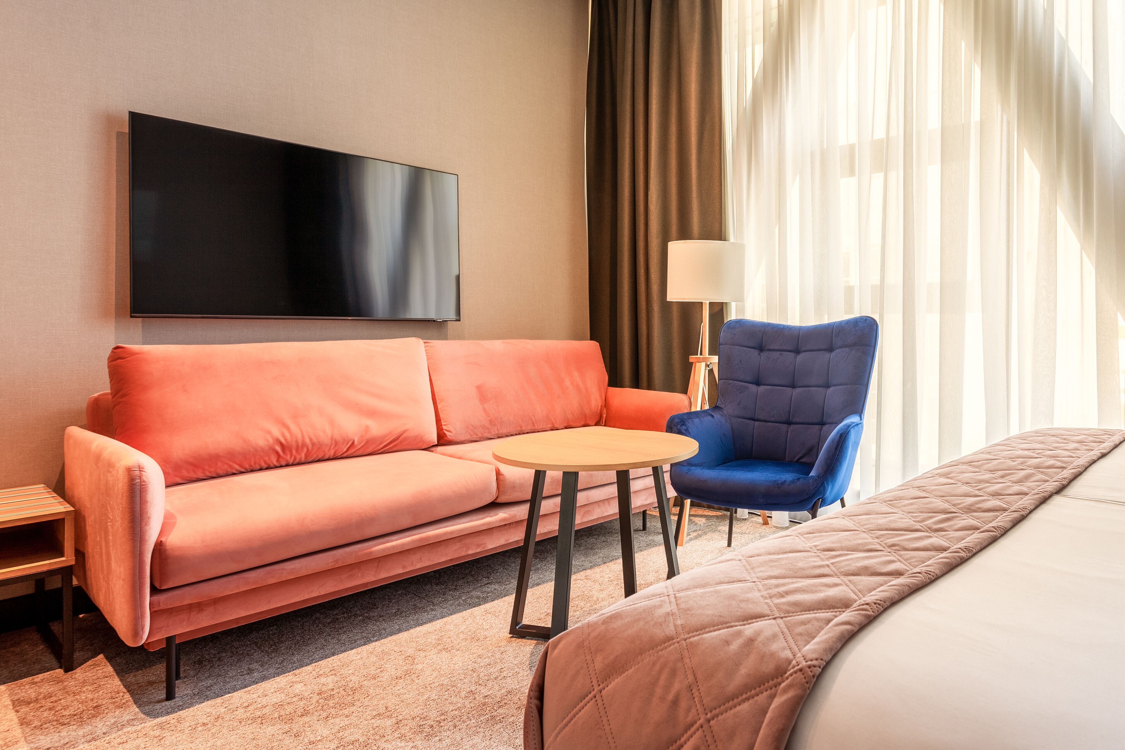 Habitación de hotel con cama, sofá, sillón, televisor y lámpara.