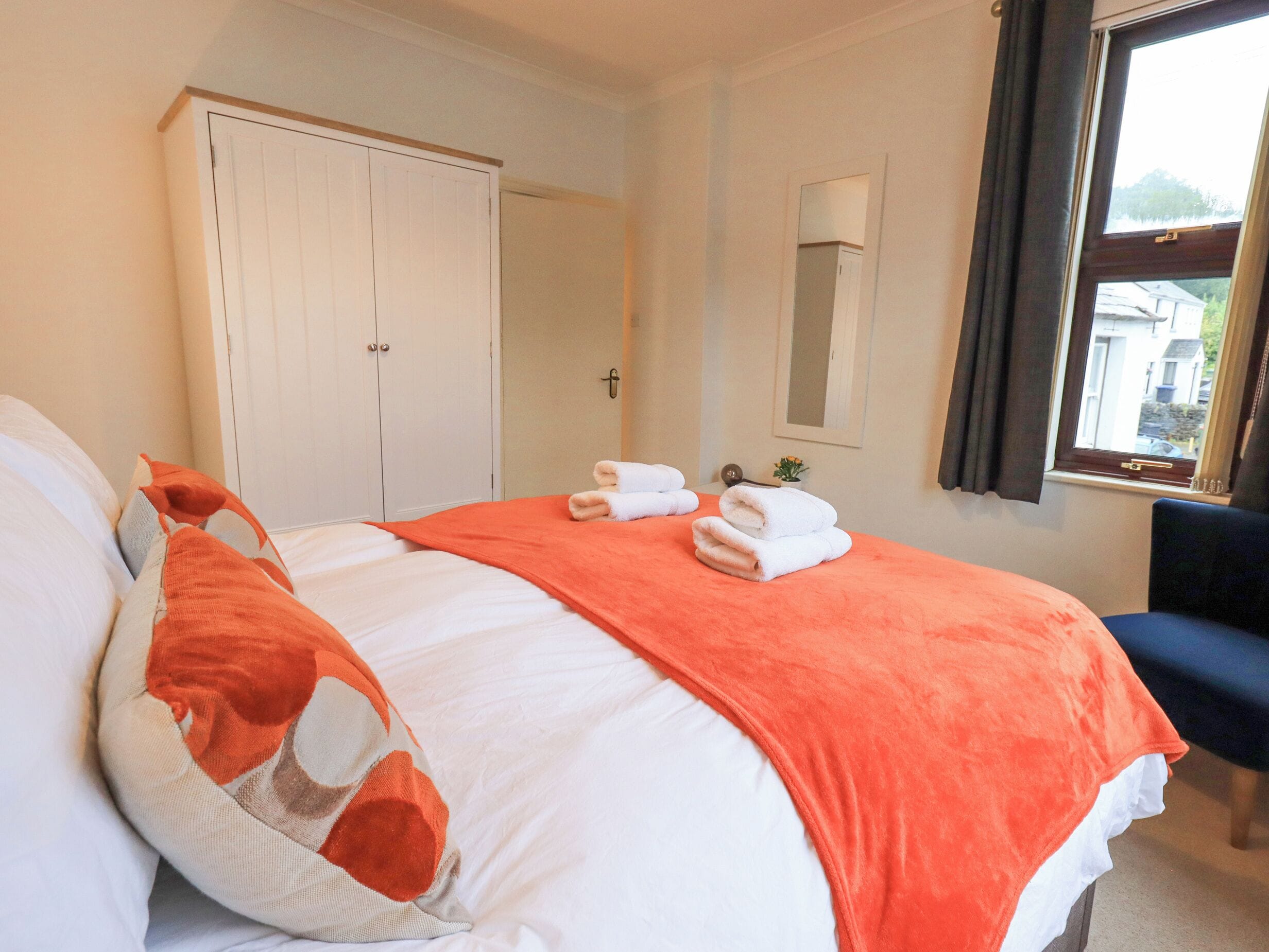 A hotel room with a bed, a wardrobe, a mirror, and a window with curtains.