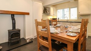 A dining area with a wooden table set for four, surrounded by wooden chairs. A black wood stove is positioned to the left of the table. - Holme Rigg (Keswick)