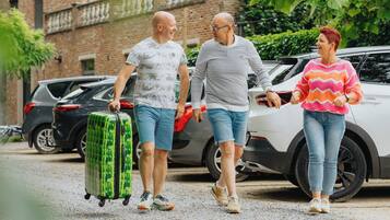 Drie personen lopen met een koffer, met een auto op de achtergrond.