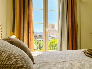 A hotel room with a bed, a lamp, and a view of a building through large windows. - Diamond Suite Luxury Penthouse (Granada)