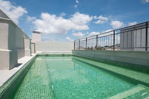 Ein Dachpool mit klarem, blauem Wasser, umgeben von einem weißen Gebäude und einem Metallgeländer.