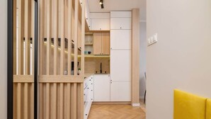 A modern kitchen with wooden cabinets, a herringbone floor, and a yellow accent wall. - Cozy Studio | In the Heart of Kazimierz, Close to Wawel Castle (Kraków)