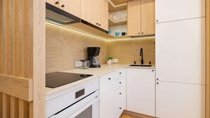A modern kitchen with light wood cabinetry, a black stove, and a coffee maker. - Cozy Studio | In the Heart of Kazimierz, Close to Wawel Castle (Kraków)