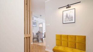 A hallway with a yellow bench, a framed picture on the wall, and a dining area in the background. - Cozy Studio | In the Heart of Kazimierz, Close to Wawel Castle (Kraków)