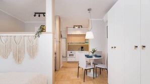 A modern kitchen with wooden cabinets, a dining area with a white table and chairs, and a hanging macrame wall decoration. - Cozy Studio | In the Heart of Kazimierz, Close to Wawel Castle (Kraków)