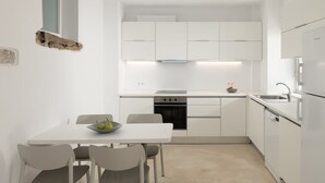 Una cocina moderna con armarios blancos, una mesa de comedor con sillas, un horno empotrado y un lavavajillas.