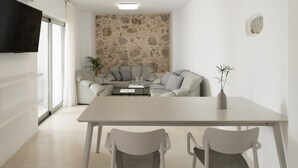 A modern living room with a stone wall, a sofa, a dining table with chairs, and a flat-screen TV mounted on the wall.