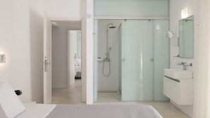 A modern hotel room with a bed, a bathroom with a glass shower enclosure, and a white sink.