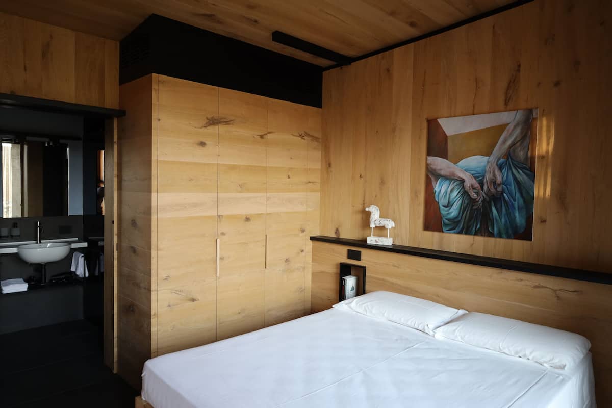 A wooden-paneled room with a bed, a painting, a sink, and a small cabinet.