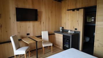 Une chambre moderne avec des murs en bois, un téléviseur à écran plat fixé au mur, un petit coin cuisine équipé d’un évier et d’un plan de travail, et un lit avec une literie blanche.