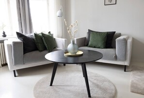 Uma sala de estar moderna com dois sofás cinza, uma mesa de centro redonda preta e um vaso com plantas secas.