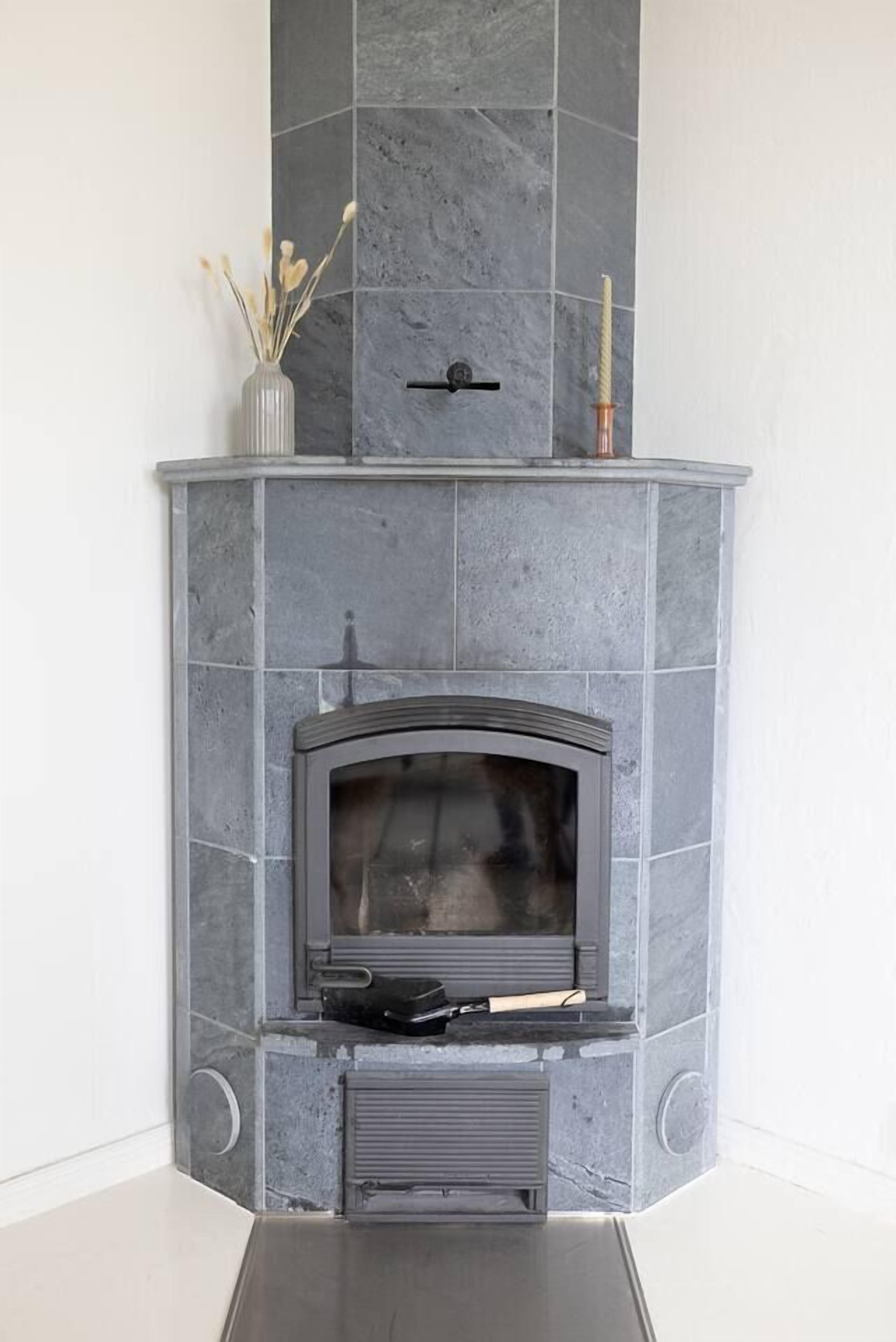 Una chimenea en esquina con revestimiento de piedra, puerta de cristal y un estante pequeño en la parte superior.