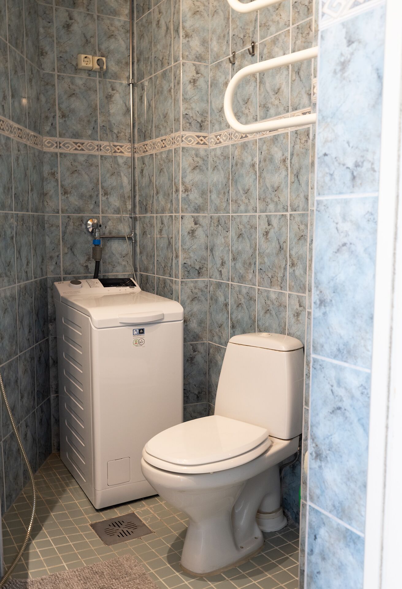 A compact bathroom with a white toilet, a wall-mounted washing machine, and a shower area.