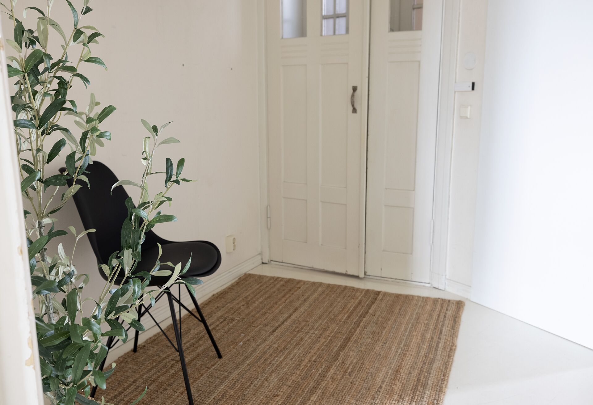 Een kamer met een zwarte stoel, een geweven vloerkleed en een witte deur.