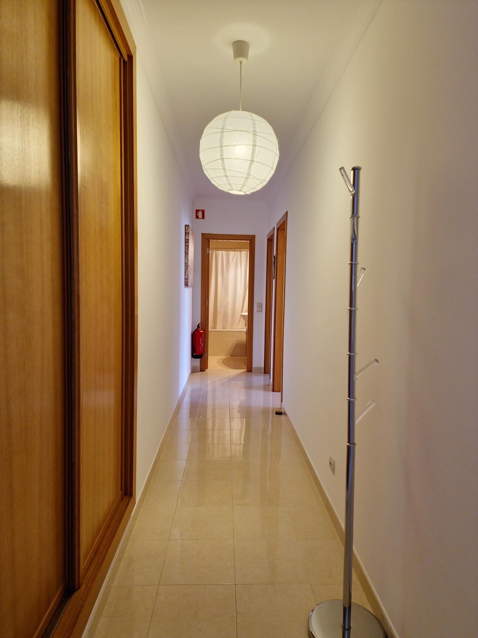 A minimalist room with a wooden floor, a large window, and a hanging light fixture.
