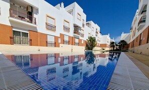 A swimming pool with blue tiles, surrounded by white and red buildings with balconies.
