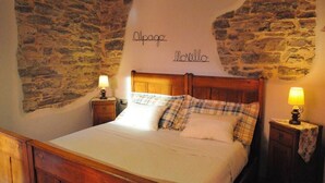 Una camera da letto con parete in pietra, struttura letto in legno e due comodini con lampade.