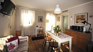 Un accogliente soggiorno con divano, tavolo da pranzo e sedie. C'è una TV a muro, una lampada e un forno a microonde sul bancone.