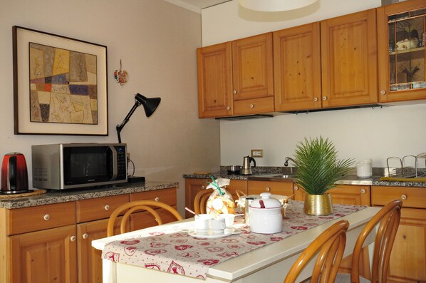 A kitchen with wooden cabinets, a microwave, a coffee maker, and a dining table set for two. - Lovely flat with garden (Feltre)