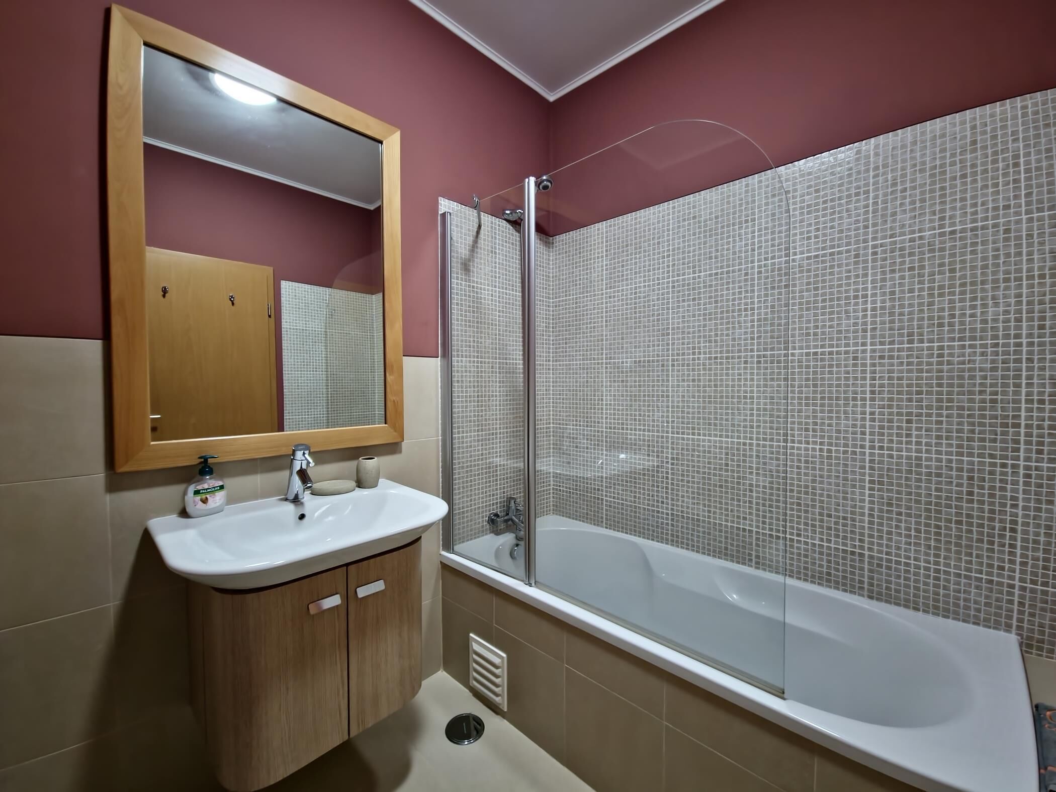 A bathroom with a wooden vanity, a white sink, a mirror, and a bathtub with tiled walls.
