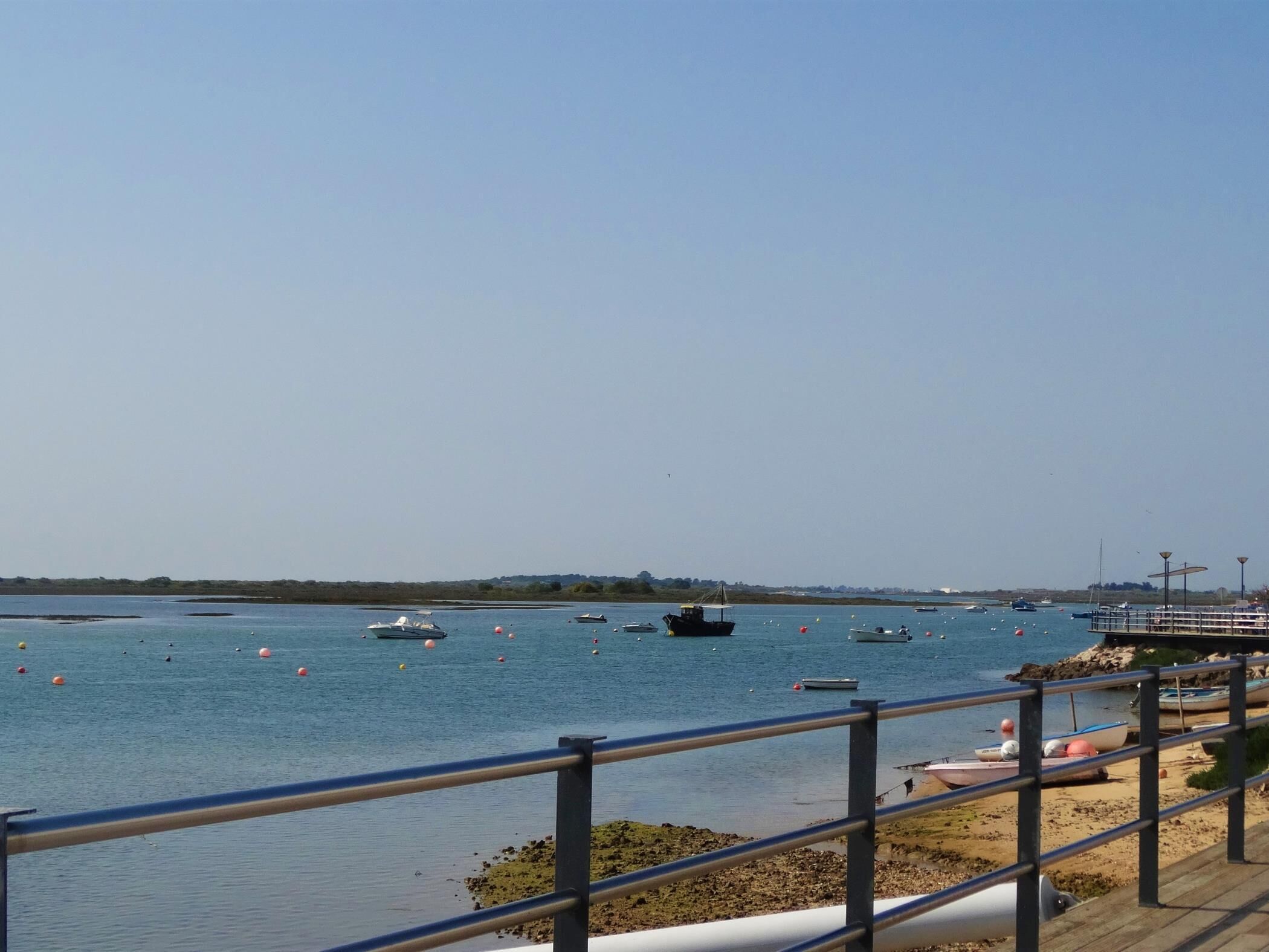 Vista costera con cielo despejado, un muelle de madera y varias embarcaciones en el agua.