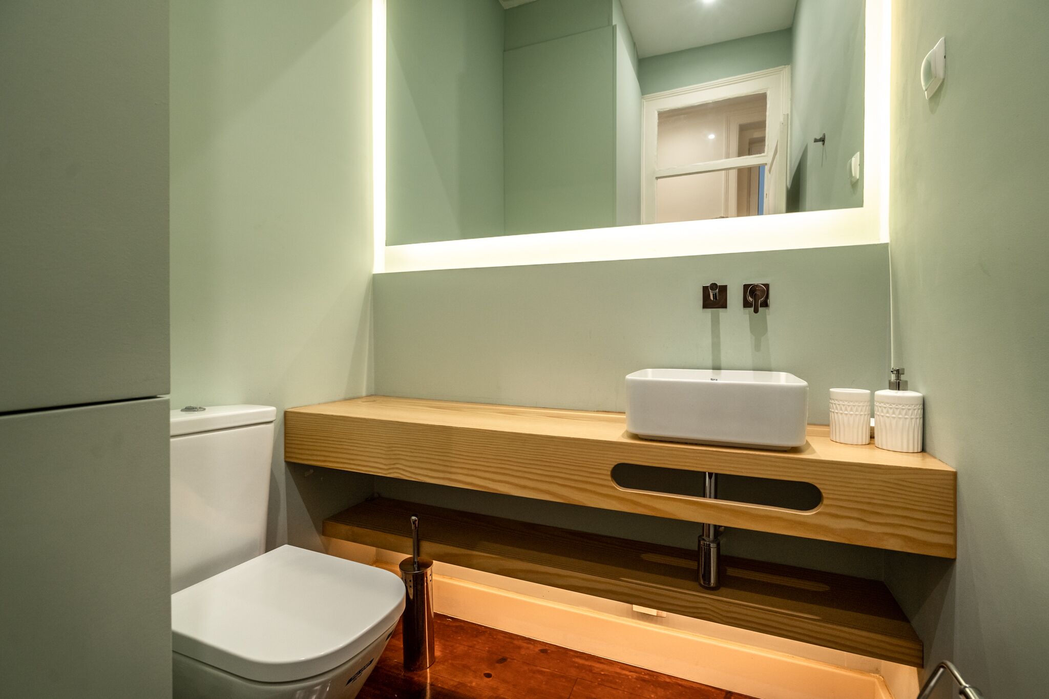 A modern bathroom with a white toilet, a wooden vanity with a white sink, and a mirror above the vanity.