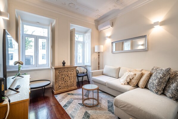 Uma sala de estar com sofá, mesa de centro, televisão e aparador decorativo.