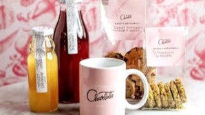Una taza rosa con la palabra 'Charlotte', una botella de miel, un tarro de miel y un paquete de galletas.