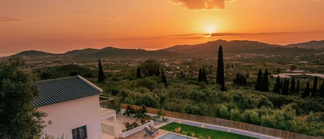 A pool area with a view of the sunset over a hilly landscape.