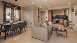 Ein modernes Wohnzimmer mit einer Couch, einem Esstisch und Stühlen. Es gibt eine Küchenzeile mit Holzschränken und einer Arbeitsplatte.