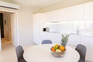Una cocina moderna con armarios blancos, una mesa redonda y un frutero sobre la mesa.