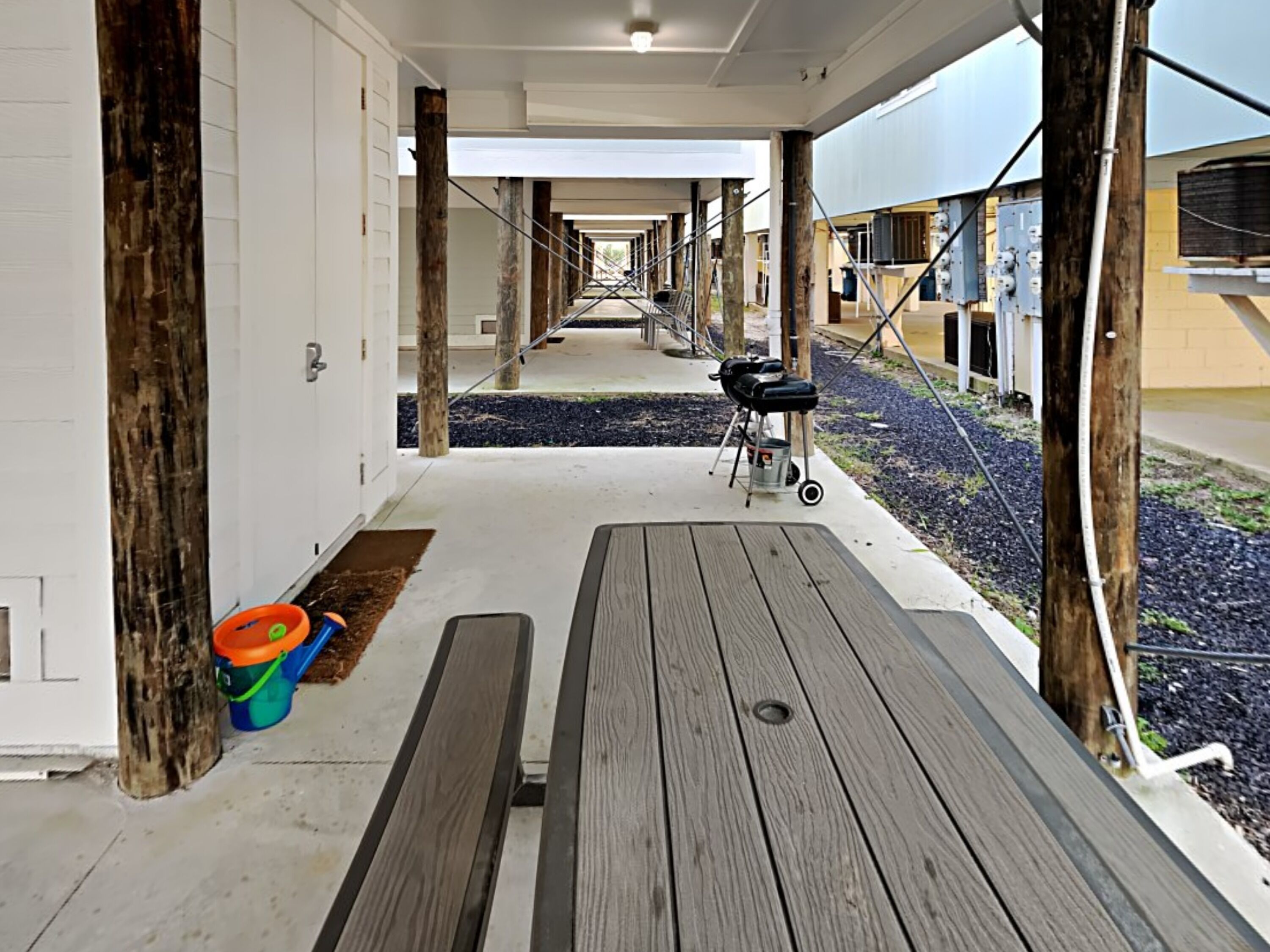 A covered outdoor area with a wooden bench, picnic table, and barbecue grill.