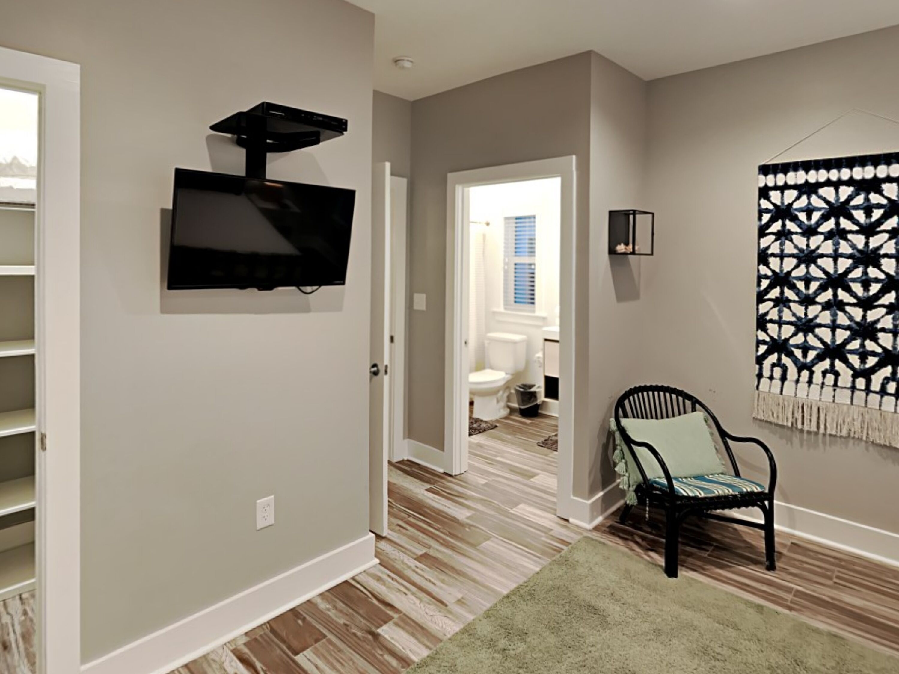 A modern living room with a flat-screen TV mounted on the wall, a patterned wall hanging, and a chair with a cushion.