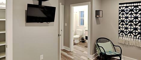 A modern living room with a flat-screen TV mounted on the wall, a patterned wall hanging, and a chair with a cushion.