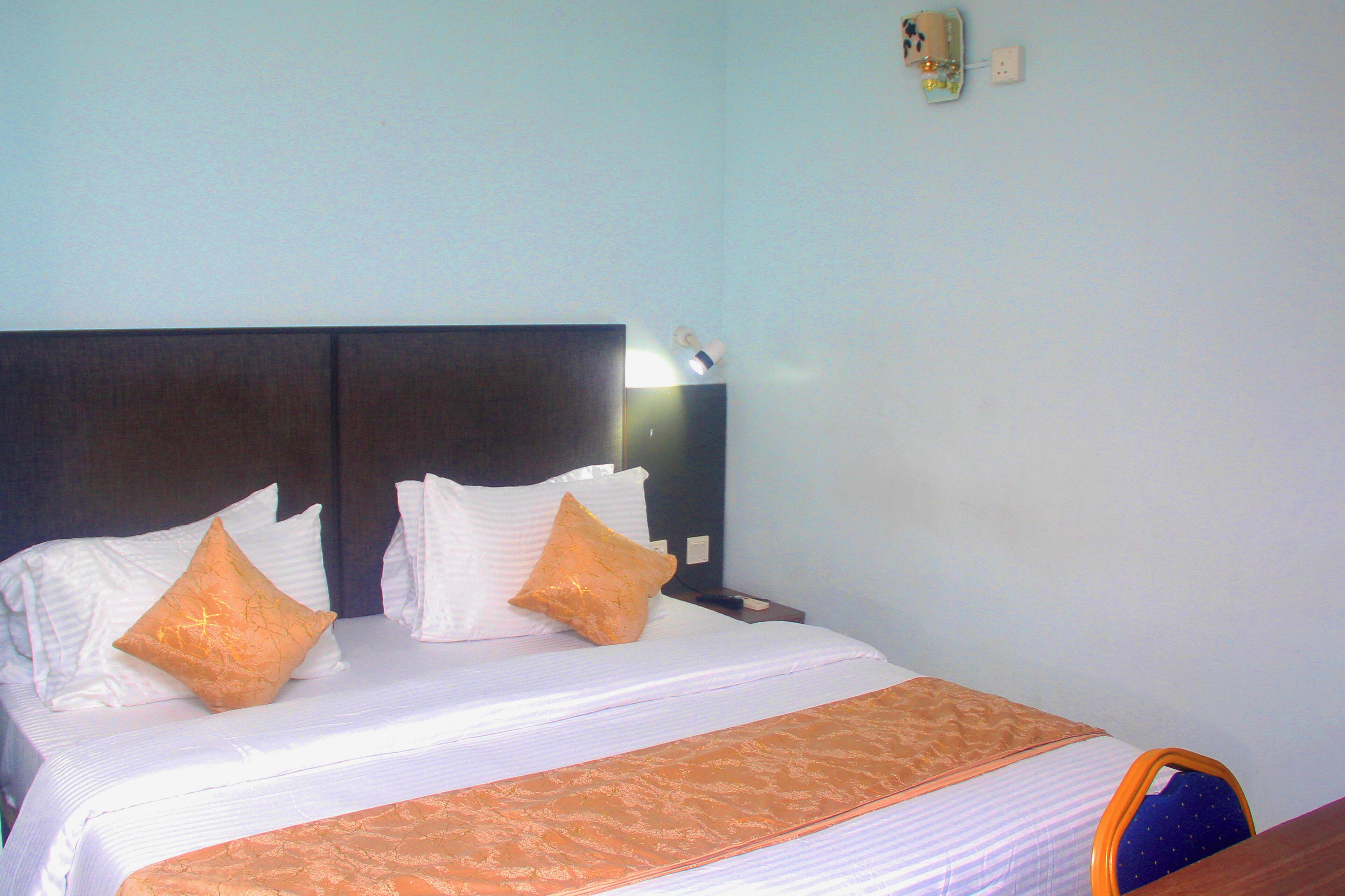 A neatly made bed with white linens and two orange pillows, a wooden headboard, and a blue chair with a patterned seat.