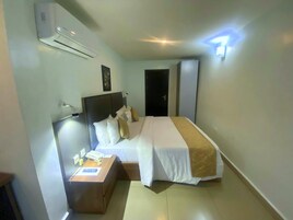 Una habitación de hotel con cama, mesita de noche, lámpara y aire acondicionado.