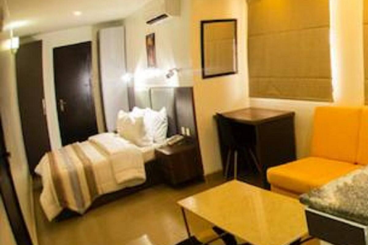 A compact hotel room with a bed, a small table, a sofa, and a window with blinds.