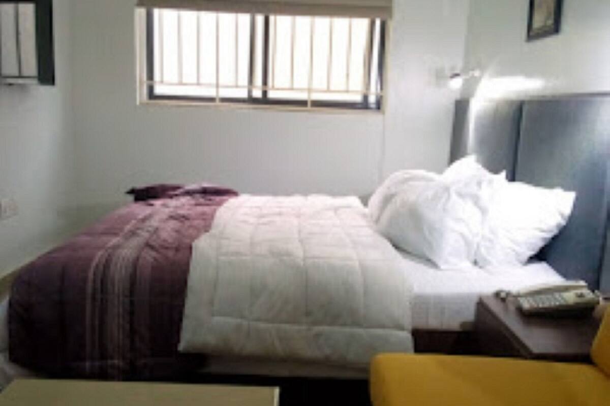A bedroom with a bed, a nightstand, a chair, and a window.